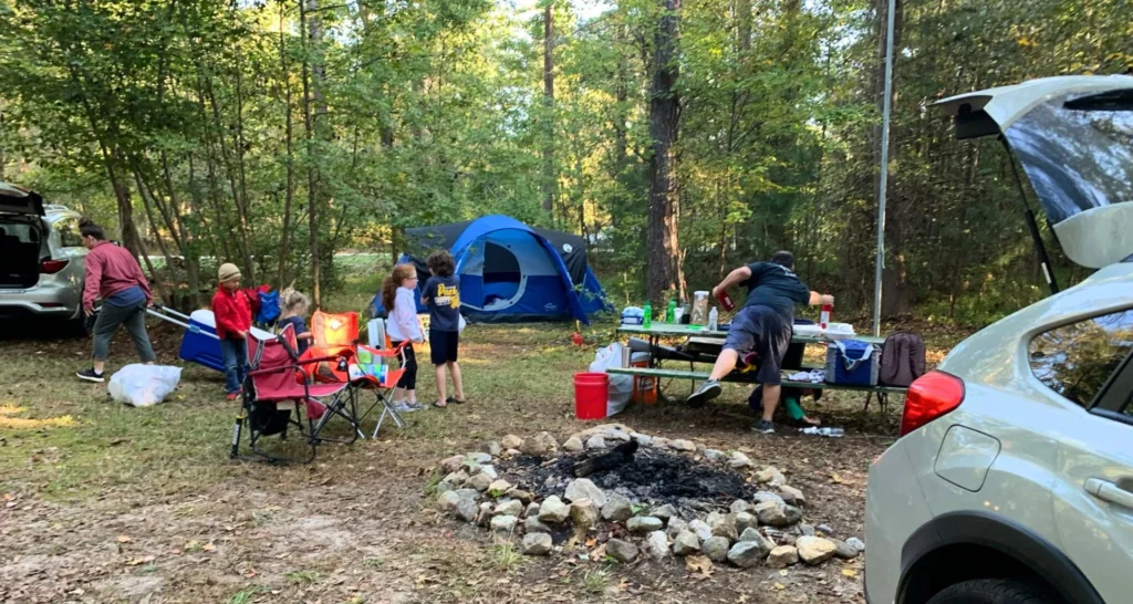 Father setting up a family campsite while several children sit in camp chairs around a fire ring