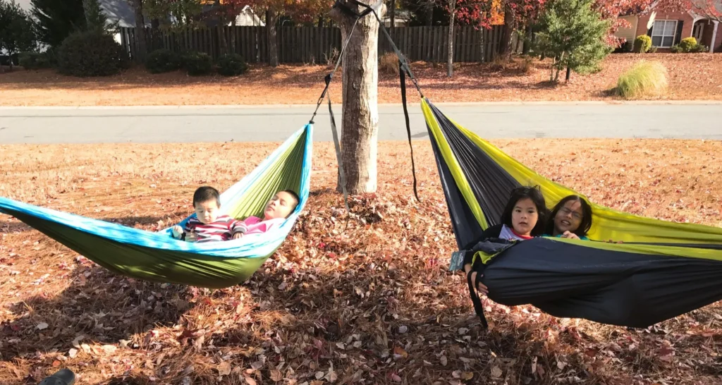 Two hammocks in the front yard with kids testing them before a family camping trip