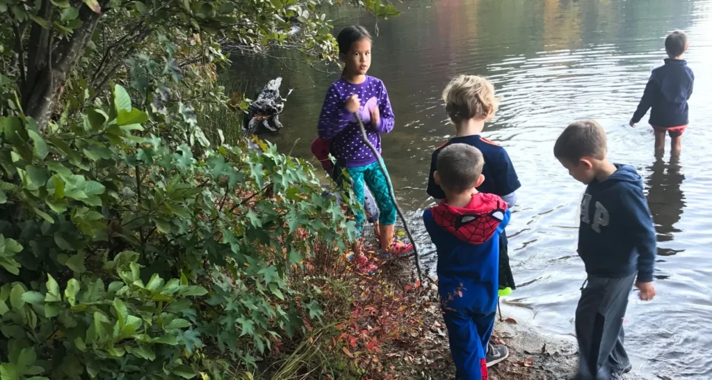 Five kids wading at the edge of a lake during a family camping trip